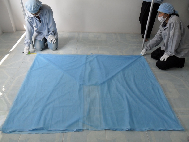 Two staff wearing protective equipment inspecting a bed net.